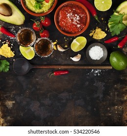 Mixed mexican food background. Party food. Guacamole,nachos, salsa, peppers, tomatoes, avocado and tequila shots on a rustic table.Tex-mex cuisine. Assorted appetizers. Food frame