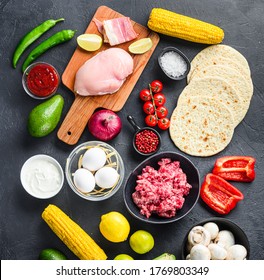 Mixed mexican food background, raw organic ingredients for tacos with chicken and beef meat, corn tortilla, salsa, chilli over black background, top view square.