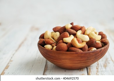 Mixed nuts in a  bowl on a white wooden background. 