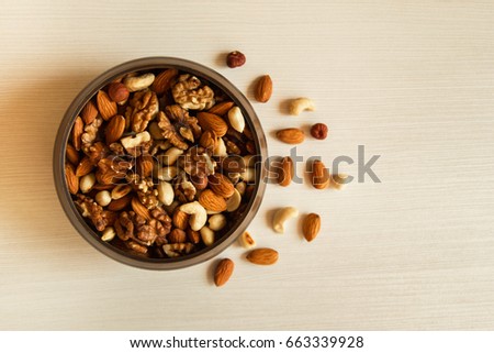 Mixed nuts in a metal brown bowl on a white wooden background.