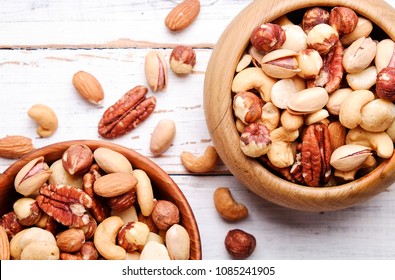 Mixed nuts in wooden bowl and scattered on table. Trail mix of pecan, almond, macadamia & brazil edible nuts with walnut hazelnut on wood textured surface. Background, copy space, top view, close up. - Shutterstock ID 1085241905