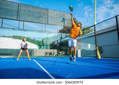 Mixed padel match in a blue grass padel court - Beautiful girl and handsome man playing padel outdoor - Shutterstock ID 2066283974