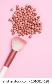 Mixed pink and tan colored glow face pearls blush and brush on pink background. Top view point.