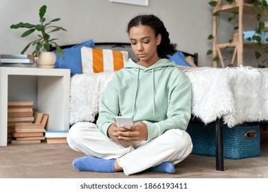 Mixed Race African American Gen Z Teenage Girl User Using Mobile Cellphone Social Media Apps, Teenager Texting, Chatting With Friends Online Holding Smart Phone Tech Sitting In Bedroom At Home.