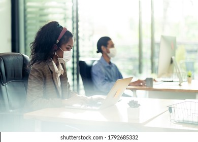 Mixed Race Of African Black And Asian Businesswoman Office Worker Wear Face Mask Working In New Normal Office With Social Distance To Colleague In Background Prevent Coronavirus COVID-19 Spreading.