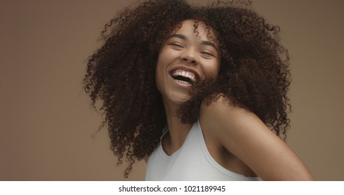 mixed race black woman portrait with big afro hair, curly hair in beige background. Natural laughing