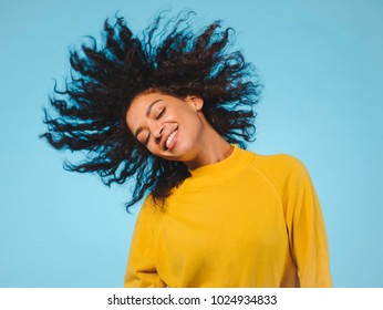 mixed race black woman portrait with big afro curly hair on blue background dancing and with hairstyle flying in air