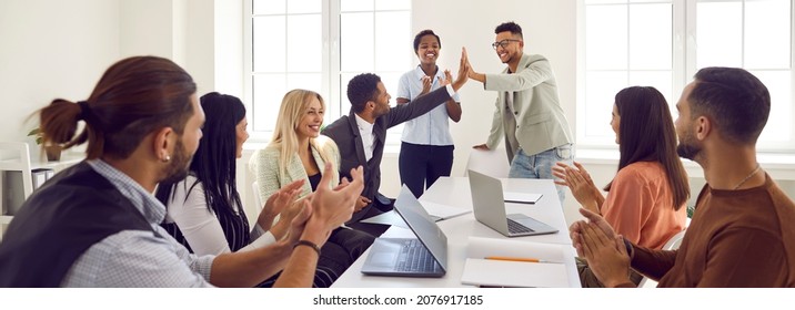 Mixed race business team celebrating good results in office meeting. Happy young black man gives high five to coworker while diverse multi ethnic teammates are applauding. Teamwork and success concept