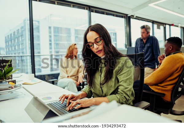 Mixed\
race business woman typing on keypad researching digital designs\
for new advertising project sitting in fancy\
office