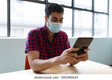 Mixed race businessman wearing face mask using tablet sitting at table. social distancing health protection hygiene in workplace during covid 19 pandemic. - Powered by Shutterstock