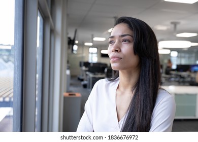 Mixed race businesswoman working in a modern office, standing and looking out of the window in thought. Social distancing in workplace during Coronavirus Covid 19 pandemic. - Shutterstock ID 1836676972