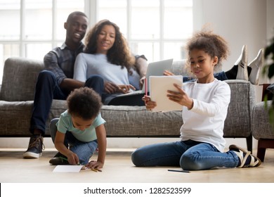 Mixed race children playing drawing and colored pencils warm floor while happy african parents relax couch in living room  cute kids siblings having fun at home  black family leisure time