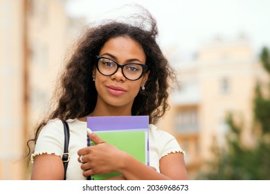 Mixed Race College Student Girl In Stylish Glasses Hold Books Outdoor Campus. Portrait Cheerful African American Young Woman. Dark Skinned Female With Loose Wavy Curls