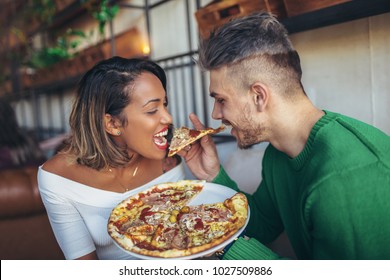 Mixed Race Couple Eating Pizza In Modern Cafe. They Are Laughing And Eating Pizza And Having A Great Time.