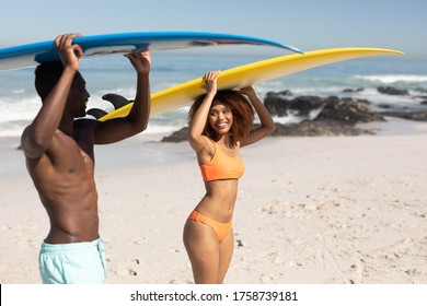 A mixed race couple enjoying free time on beach on a sunny day together, surfing, carrying their surfboards, having fun with sun shining on their faces. - Powered by Shutterstock