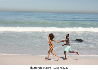 A Mixed Race Couple Enjoying Free Time On Beach On A Sunny Day Together, Running And Holding Each Others Hands With Sun Shining On Their Faces.