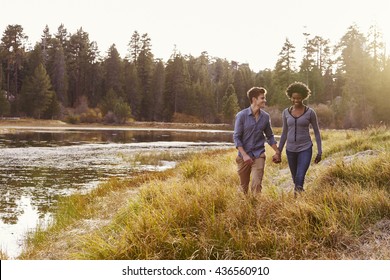 Mixed Race Couple Holding Hands, Walking Near A Rural Lake