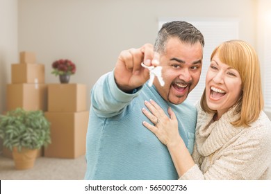 Mixed Race Couple Holding House Keys Inside Empty Room With Moving Boxes.