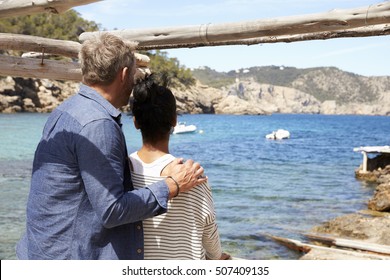 Mixed Race Couple Looking Out To Sea From A Jetty, Back View