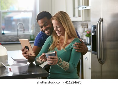 Mixed race couple looking at a tablet computer together in kitchen - Powered by Shutterstock