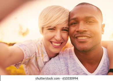 Mixed race couple of millennial in a grass field taking a selfie with a smartphone - Powered by Shutterstock