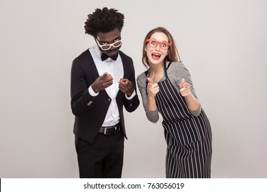 Mixed Race Couple Pointing Fingers At Camera And Smiling. Studio Shot, Gray Background