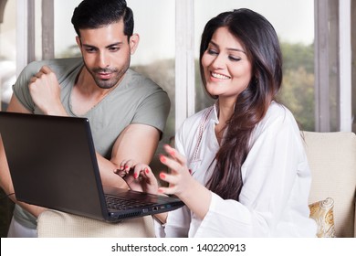 Mixed Race Couple Using The Laptop Sitting On A White Sofa.