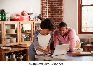 Mixed Race Couple Using Laptop Computer In Their Kitchen