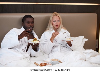 Mixed Race Couple Watch Tv And Have Meal In Hotel, Lovely Woman And Man In Bathrobe Enjoy Time In Luxurious Hotel