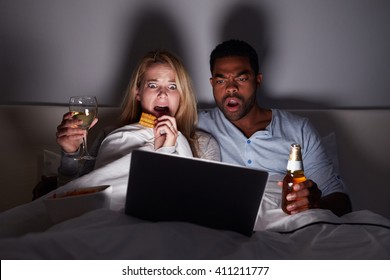 Mixed Race Couple Watching Scary Film In Bed On Laptop