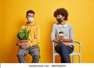 Mixed race couple wear protective face masks keep distance look at each other prevent coronavirus spread pose on chairs against yellow background. Quarantine social distancing self isolation concept - Powered by Shutterstock