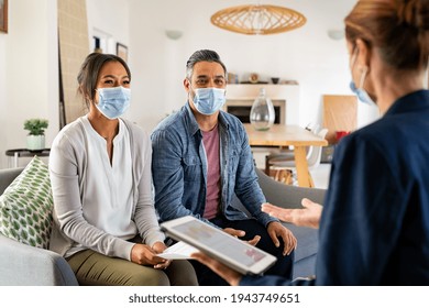 Mixed race couple wearing face mask for precaution against covid-19 and discussing deal with agent. Happy indian man and woman discussing real estate with agent wearing surgical mask.