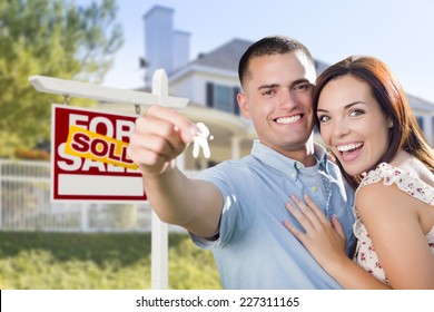 Mixed Race Excited Military Couple In Front Of New Home With New House Keys And Sold Real Estate Sign Outside.