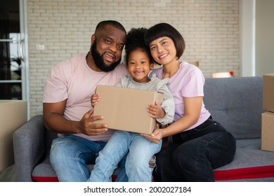 Mixed Race Families Are Sitting On The Sofa For Rest After Moving To A New House On The First Day After Buying Real Estate.  Concept Of Starting A New Life For A New Family.