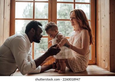 Mixed race family with dark skinned infant daughter spend time together use light window at snug apartment. African american man his fair skin wife and little girl enjoy positive emotion at home - Powered by Shutterstock