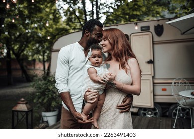 Mixed race family with dark skinned infant daughter spend time together hugs and kisses in camper park. African american man his fair skin wife and little girl enjoying summer vacation in open air - Shutterstock ID 2263491403