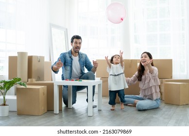 Mixed Race Family Playing Balloon Together. Young Caucasian Father With Beard, Asian Mother And Little Daughter Raised Hands Up In Air Waiting For Balloon Drop. Family Celebrate Move To New House