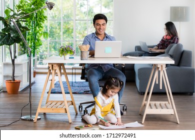 Mixed race family sharing time in living room. Caucasian father using notebook computer to work and half-Thai playing and painting under desk while Asian mother with laptop working her job on sofa.