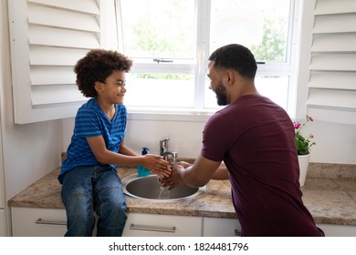 Mixed race father with son enjoying family time together at home, social distancing and self isolation in quarantine lockdown, standing in a kitchen, washing their hands