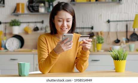 Mixed Race Female Client Holding Banking Credit Card And Smart Phone Involved In Verification Process In Mobile Application. Asian Happy Young Woman Doing Payments Online Or Shopping In Internet Store