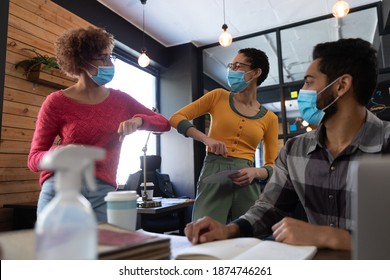 Mixed Race Female Colleagues Wearing Face Masks Elbow Bumping In Office. Hygiene In Workplace During Coronavirus Covid 19 Pandemic