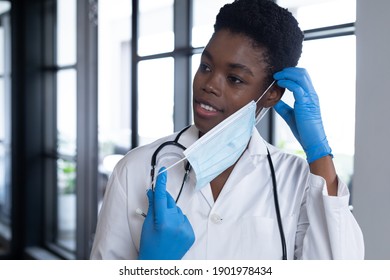 Mixed Race Female Doctor Standing Putting A Face Mask On. Medical Professional Healthcare Worker Hygiene During Coronavirus Covid 19 Pandemic.