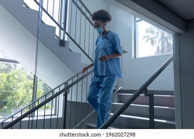 Mixed race female doctor wearing face mask and scrubs walking down stairs in hospital. medical professional at work during coronavirus covid 19 pandemic. - Powered by Shutterstock