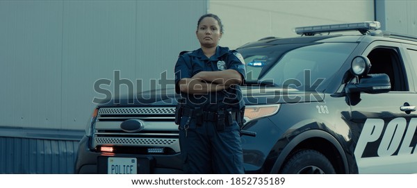 Mixed race female police officer posing against\
police car with flashing\
lights