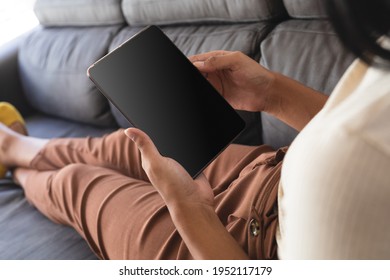 Mixed race gender fluid man relaxing at home on couch using tablet, with copy space screen. staying at home in isolation during quarantine lockdown. - Powered by Shutterstock