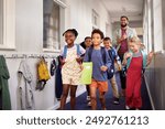 Mixed race group of classmates walking through the school hallway with male teacher at the end of the lesson. Group of multiethnic children with happy teacher running in school corridor. 