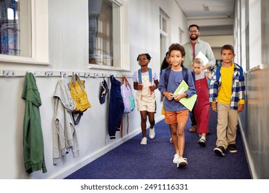 Mixed race group of classmates walking through the school hallway with male teacher. Group of multiethnic schoolchildren with teacher walking in school corridor while go to class. Cute primary pupils. - Powered by Shutterstock