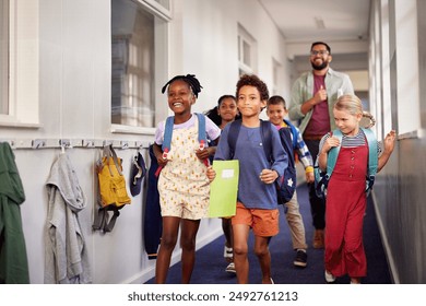 Mixed race group of classmates walking through the school hallway with male teacher at the end of the lesson. Group of multiethnic children with happy teacher running in school corridor.  - Powered by Shutterstock