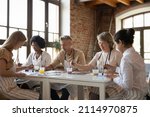 Mixed race group of different aged students drawing on art school class, painting at table, mixing colors, blending paints on palettes, enjoying artistic hobby together, talking, chatting
