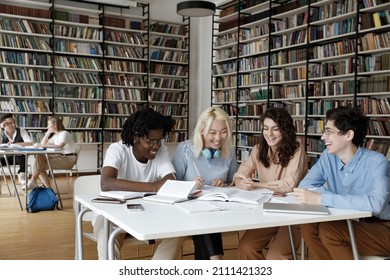 Mixed Race Group Of Students Enjoying Working Together, Collaborating On Project In University Library, Writing Notes At Table With Open Books, Discussing Research, Laughing